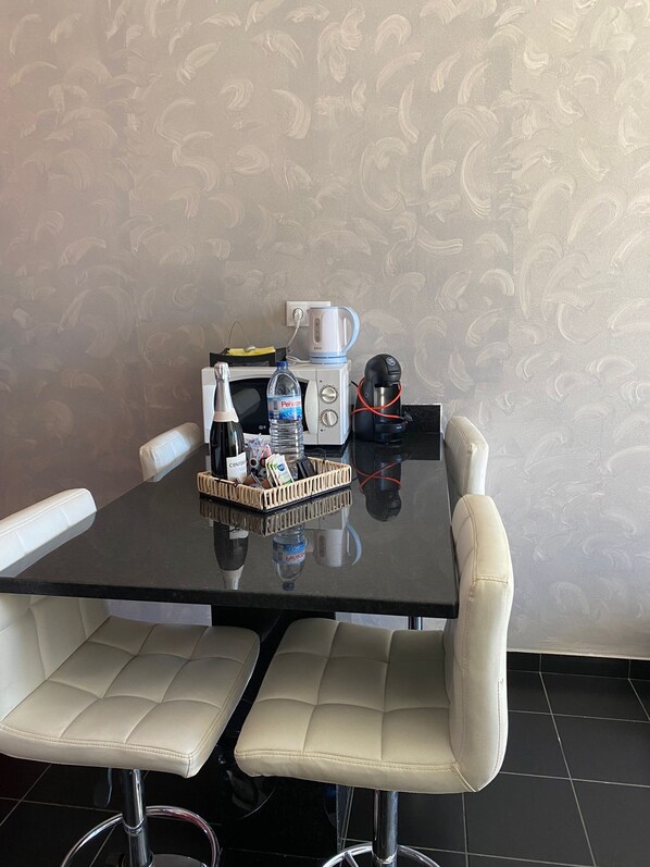A dining table with a water bottle, a coffee maker, and a basket of snacks.
