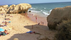 Een strand met mensen die zonnebaden en zwemmen, omringd door grote rotsformaties.
