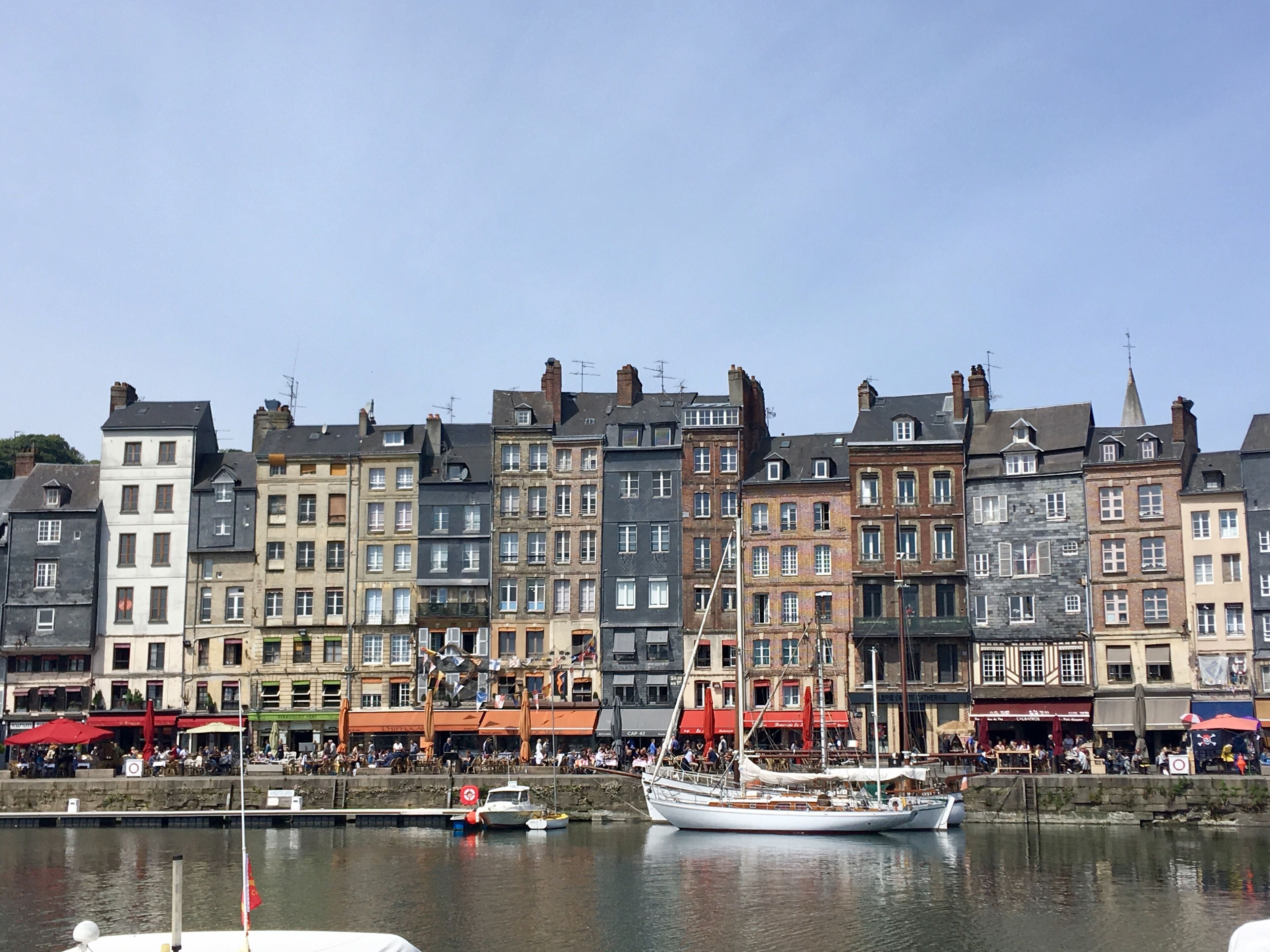 Une promenade en bord de mer bordée de bâtiments historiques, avec un voilier amarré.