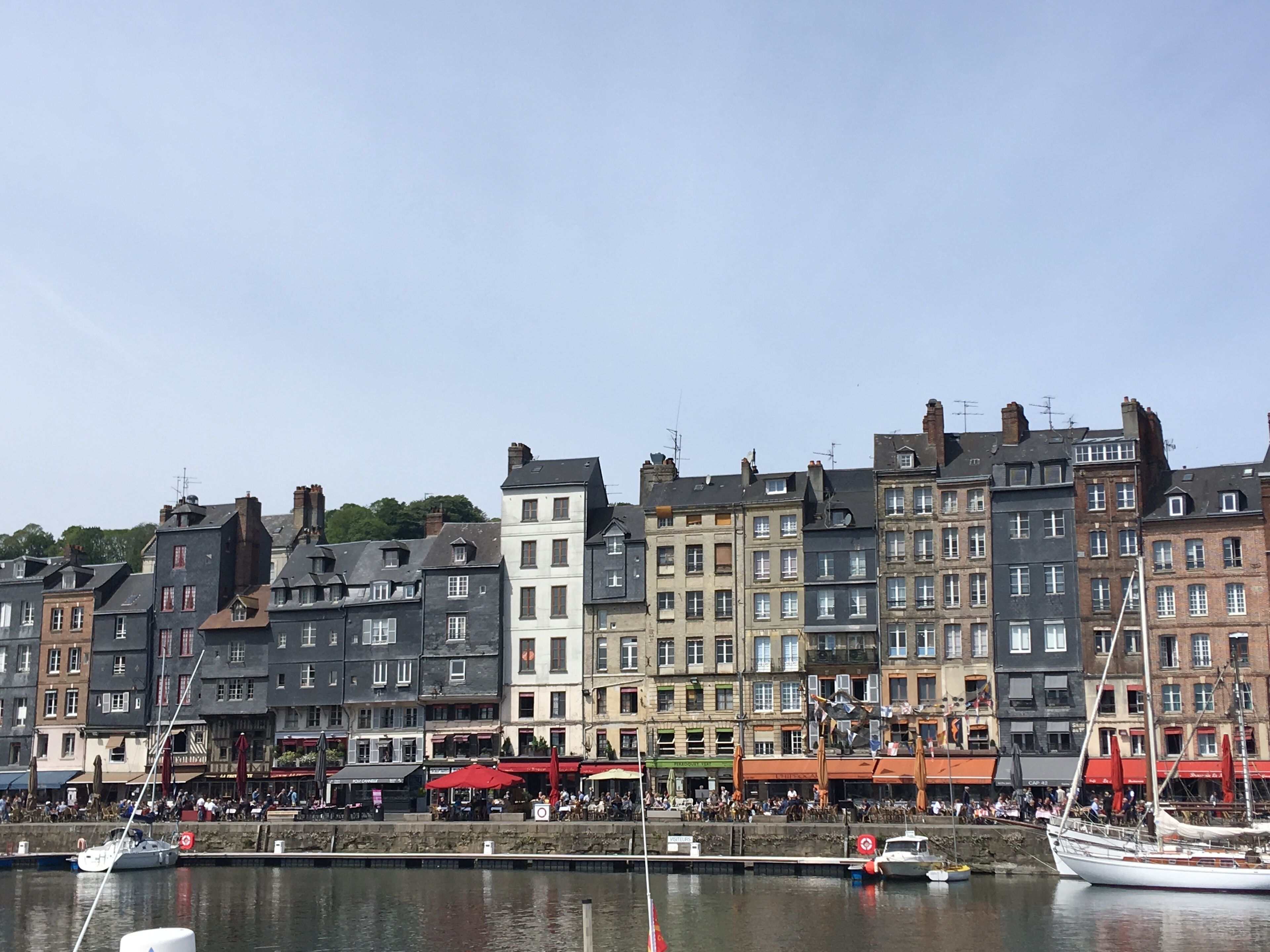 A waterfront with historic buildings, a marina with boats, and outdoor seating for cafes.