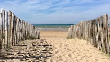 Un sentier de sable qui longe la plage et mène à l’océan, bordé de clôtures en bois.