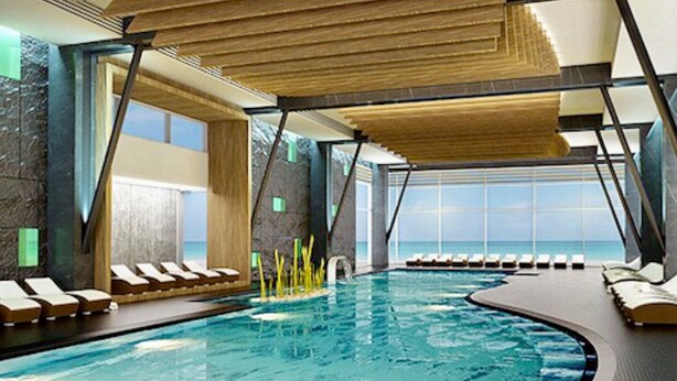 A modern indoor swimming pool with lounge chairs and a view of the ocean.