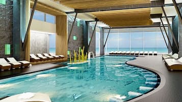 Une piscine intérieure moderne, dotée de chaises longues et offrant une vue sur l’océan.