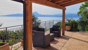A covered outdoor seating area with brick flooring and wooden beams, overlooking a body of water and distant mountains. - Small villa located in a quiet pool and sea view / Gulf of Policastro (MARATEA)