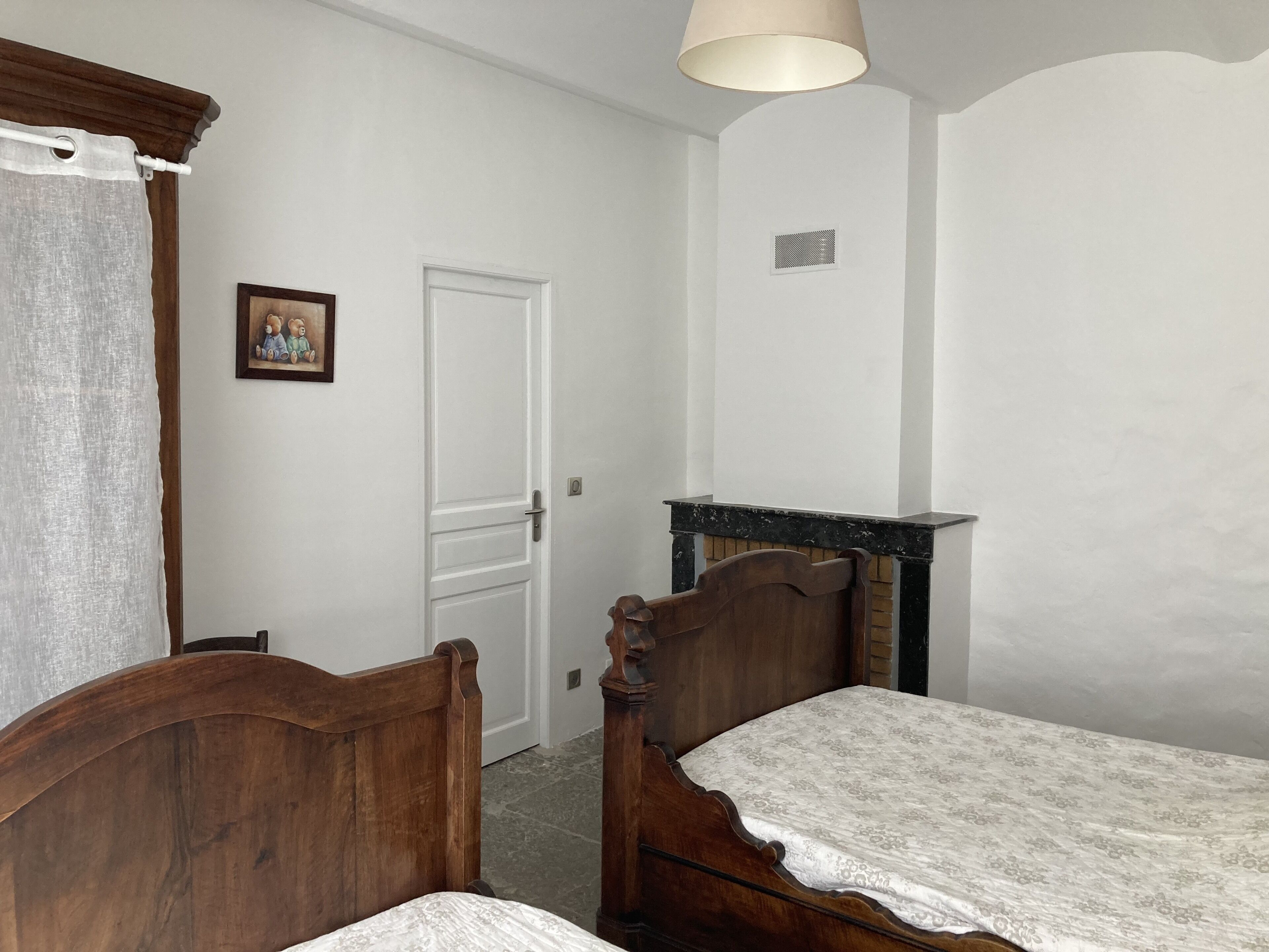 Un dormitorio con cama de madera, un tocador pequeño, una puerta y una lámpara fijada a la pared.