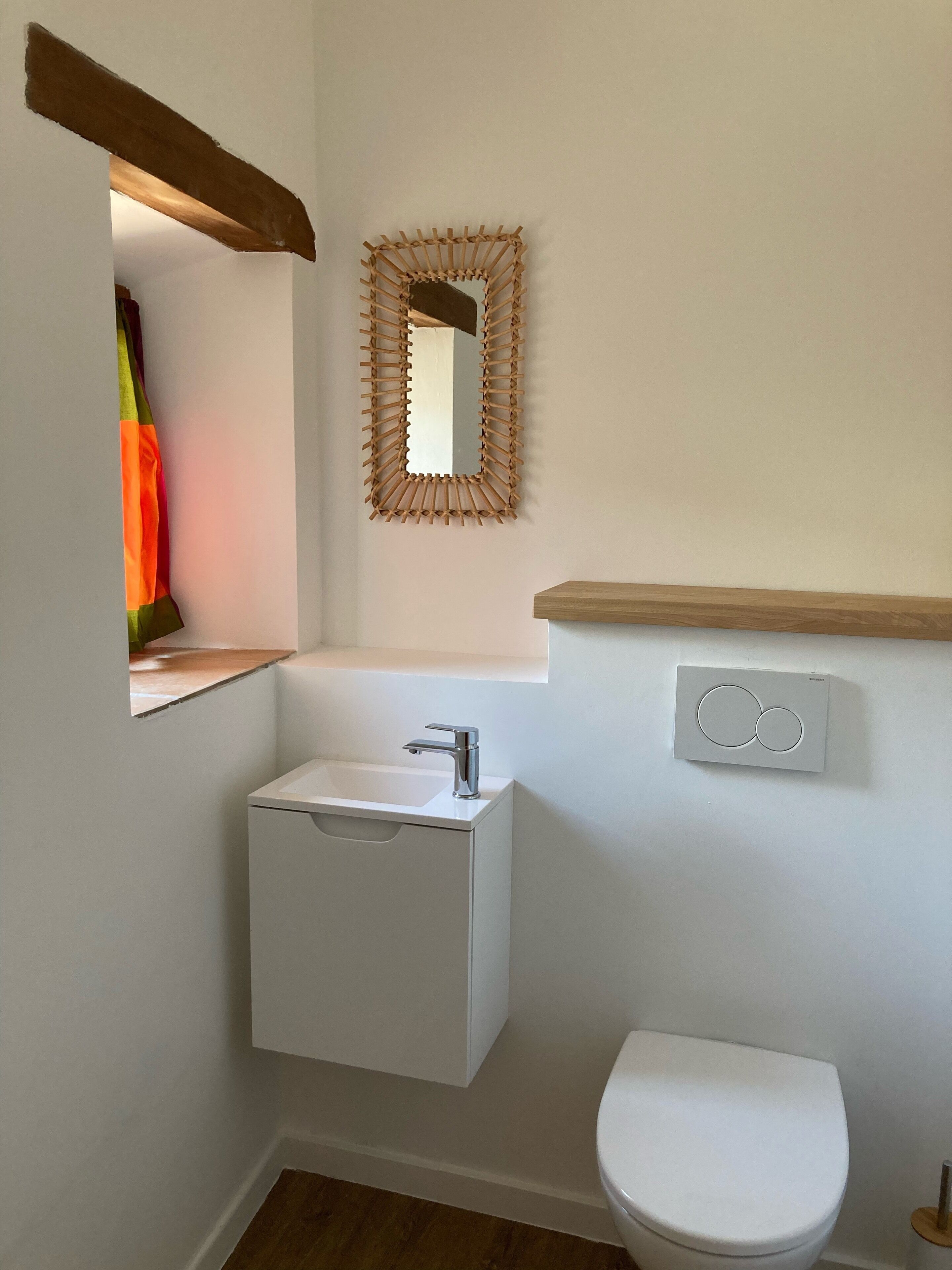 Een kleine badkamer met een wit wastafel, toilet en spiegel met gevlochten lijst.