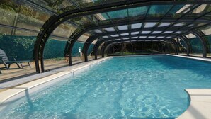 An indoor swimming pool with a glass ceiling, surrounded by a concrete deck and a few lounge chairs. - Set of houses, with heated indoor pool, surrounded by nature (Le Tablier)