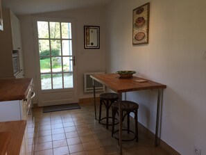 A kitchen with a wooden countertop, a dining table with stools, a window with a view of greenery, and a wall-mounted decorative plate.