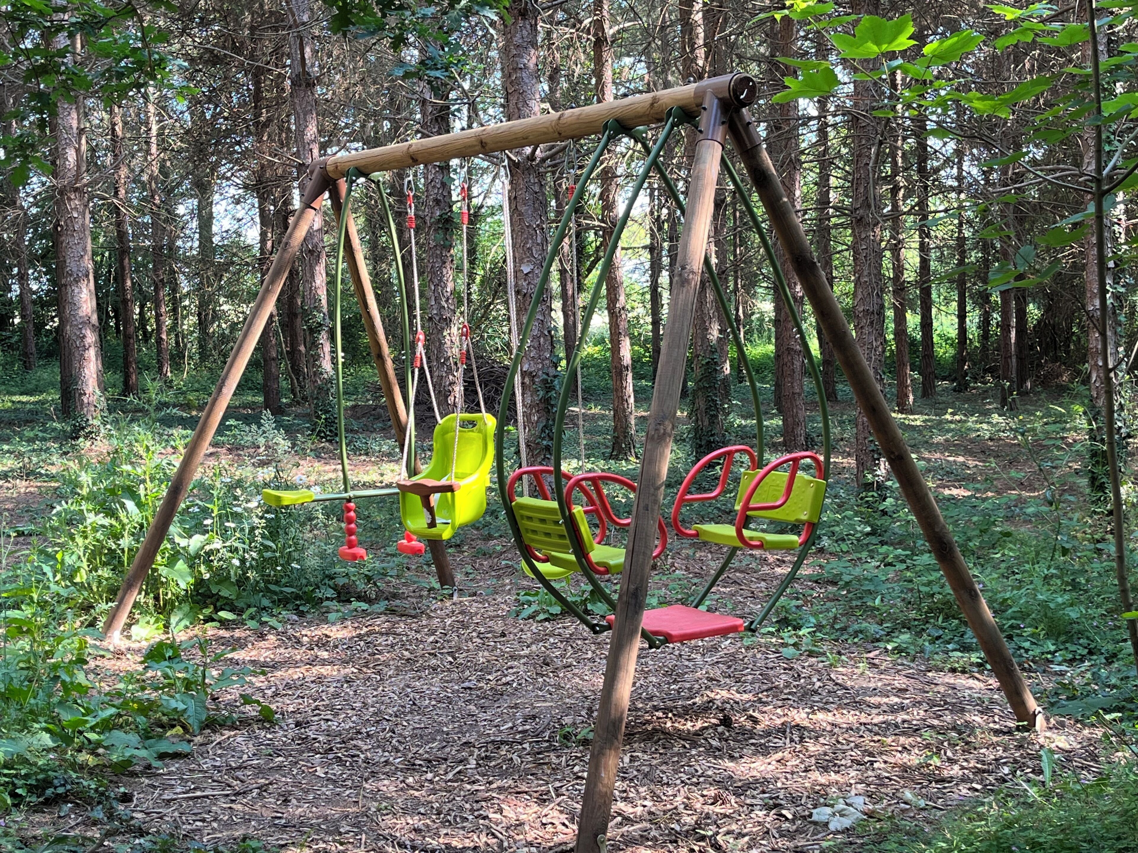 Um conjunto de baloiços numa área arborizada, com bancos e um baloiço.
