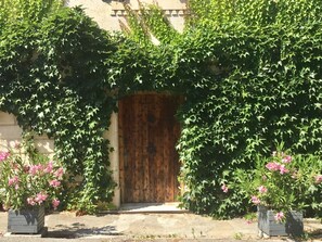 A wooden door surrounded by lush green foliage, with two flower pots on either side. - OLD BUILDING Pool, Garden and Terrace views towards GORDES and JOUCAS (Goult)