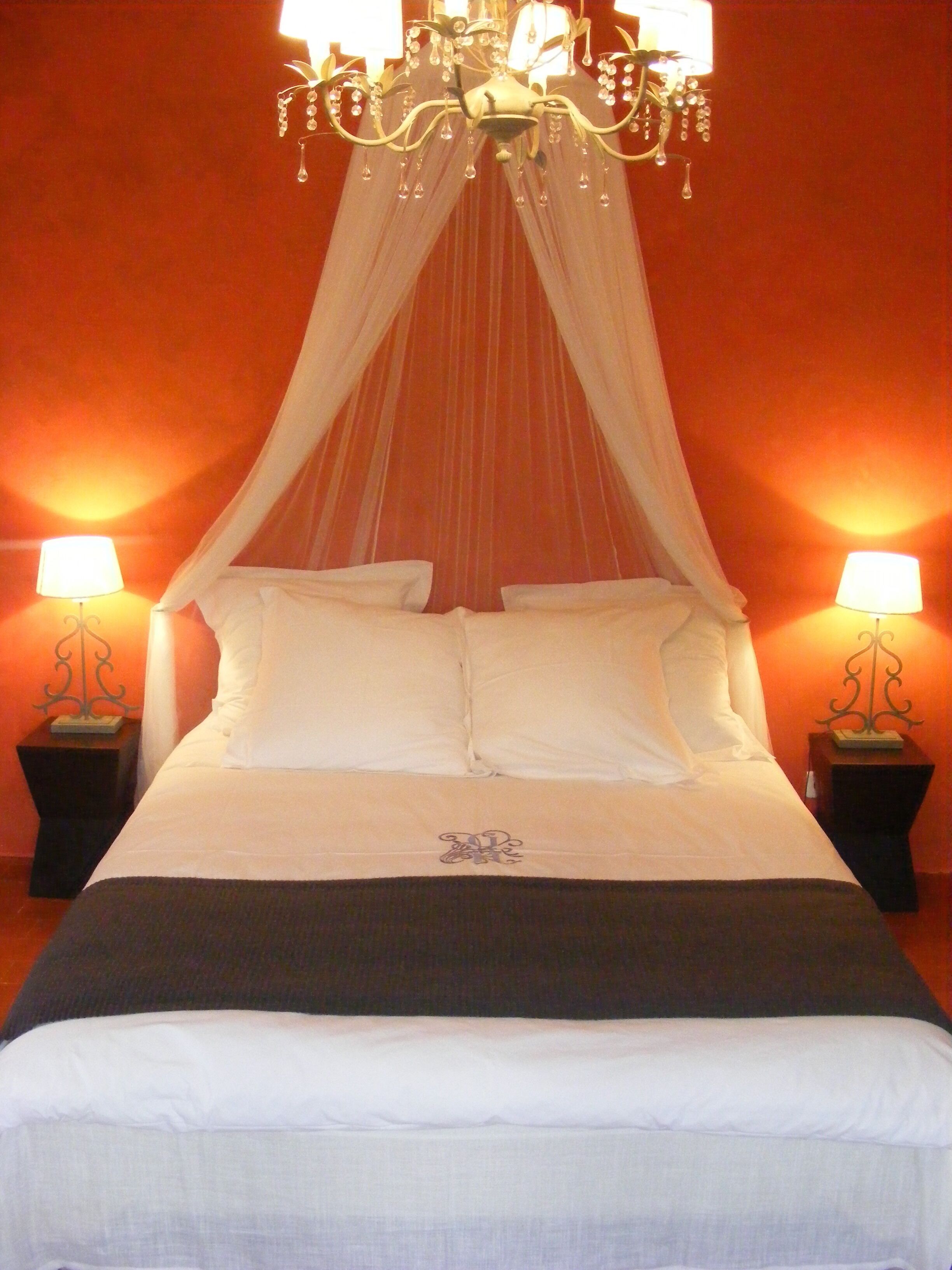 A bed with a canopy, two bedside lamps, and a chandelier.