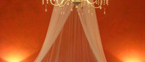 A bed with a canopy, two bedside lamps, and a chandelier.