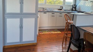 Een keuken met houten vloeren, witte kastjes en een raam dat natuurlijk licht binnenlaat.