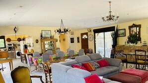 A spacious living room with a large grey sofa, a dining area with a table and chairs, and a kitchen in the background. - House near the SEA - private SWIMMING POOL - COUNTRYSIDE - in LANGUEDOC - 15 people (Loupian)