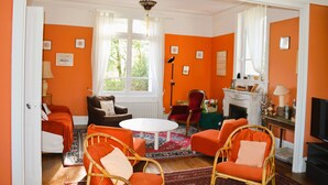 A room with orange walls, a fireplace, a television, and a dining table. - "L'école buissonière", a charming family villa between sea and marsh (La Cambe)
