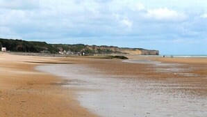 A beach with a sandy shore, a cliff in the background, and a cloudy sky. - "L'école buissonière", a charming family villa between sea and marsh (La Cambe)