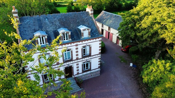 A large, historic building with multiple chimneys, a stone facade, and a paved driveway leading to a gated entrance. - "L'école buissonière", a charming family villa between sea and marsh (La Cambe)
