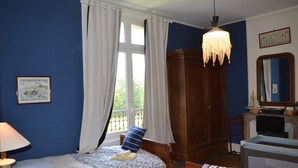 A bedroom with two beds, a wooden wardrobe, a desk with a television, and a chandelier. - "L'école buissonière", a charming family villa between sea and marsh (La Cambe)