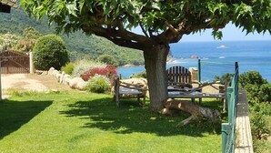 Une terrasse bordée d’arbres, avec vue sur l’océan, une clôture en bois et un banc.