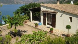 Une petite maison avec un toit en tuiles, une véranda et une vue sur un lac et des montagnes en arrière-plan.