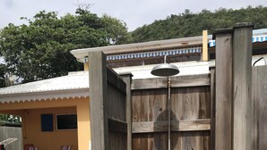A wooden structure with multiple shelves, a metal bell, and a small building with a tiled roof in the background. - Caribbean villa on the beach (LE DIAMANT)