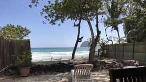 A patio with a view of the ocean, a wooden fence, a potted plant, and a white chair. - Caribbean villa on the beach (LE DIAMANT)