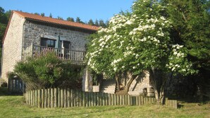 Une maison en pierre dotée d’un balcon, entourée d’une clôture en bois et d’arbres en fleurs.