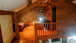 Une pièce rustique en bois, avec un mur en pierre, un lit, une petite table et un escalier menant à un niveau supérieur.