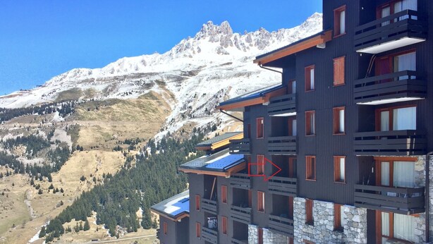 Un edificio de varios pisos con balcones, frente a un paisaje montañoso.