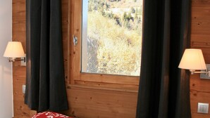 Un dormitorio con cabecera de madera, una ventana con cortinas, dos lámparas de noche y una cama con ropa de cama roja y blanca.