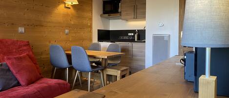 A modern kitchen with wooden cabinetry, a dining area with a wooden table and chairs, and a red sofa.