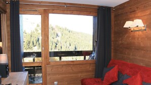 Interior de una cabaña de madera con un sofá rojo, ventanas amplias y una lámpara en la pared.
