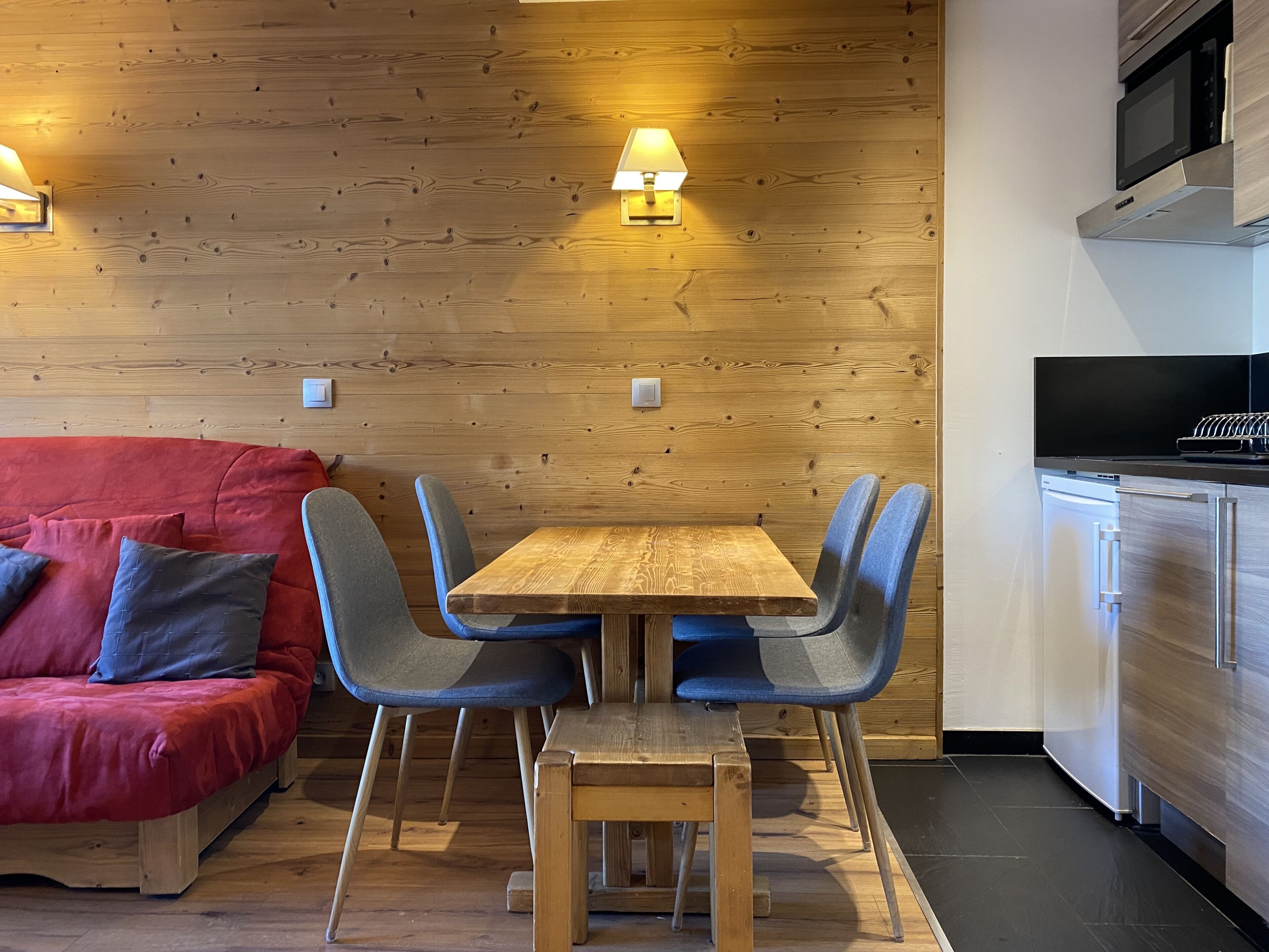 Eine moderne Küche mit Holzschränken, einer eingebauten Mikrowelle und einem Essbereich mit einem Holztisch und blauen Stühlen.