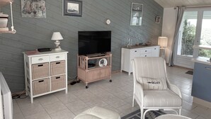 Una sala acogedora con televisión, cestos de mimbre, un sillón mullido y una ventana con cortinas.