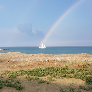 Una playa con un velero y un arcoíris a lo lejos.