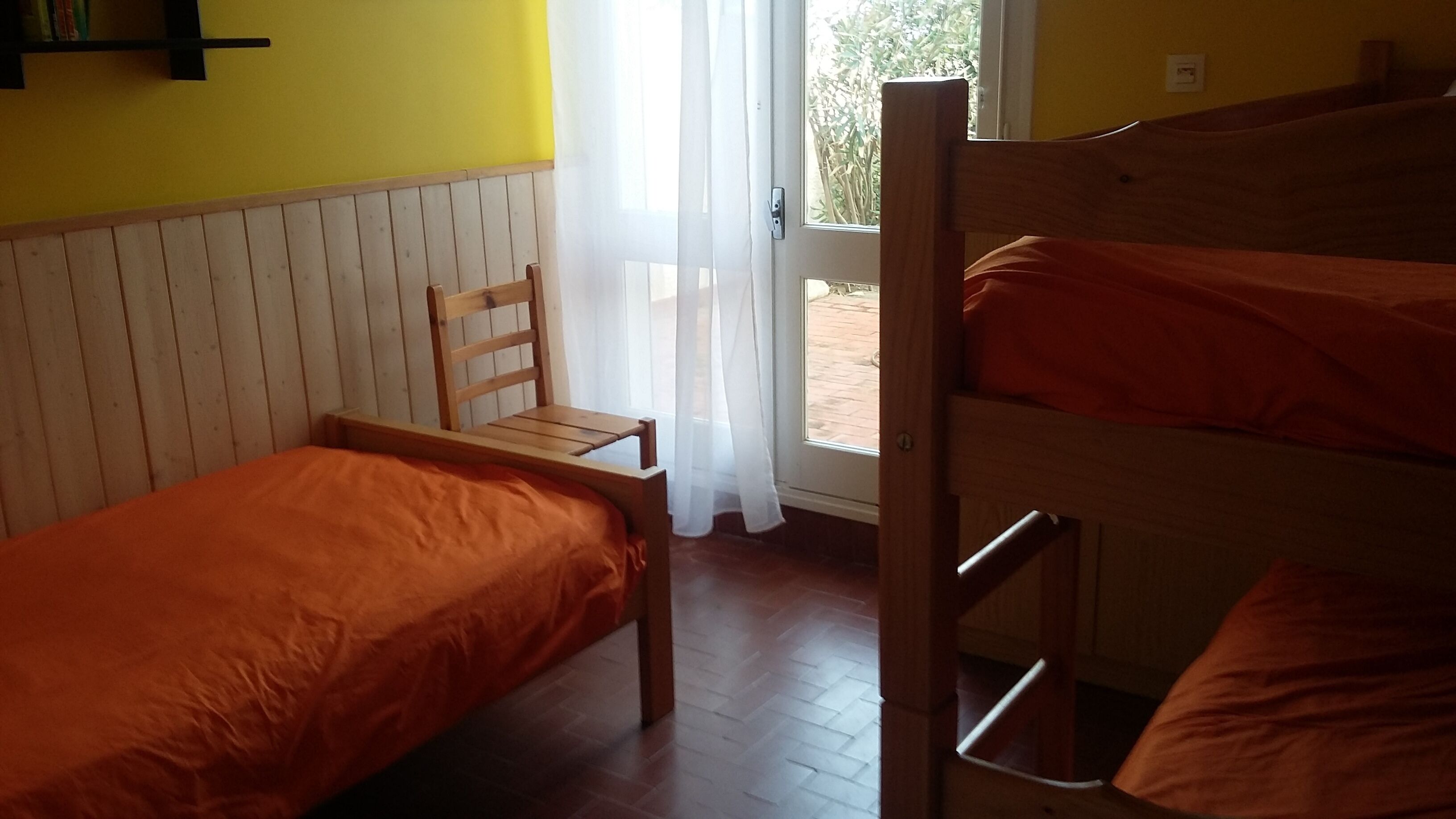 A room with two bunk beds, a wooden chair, and a window with sheer curtains.