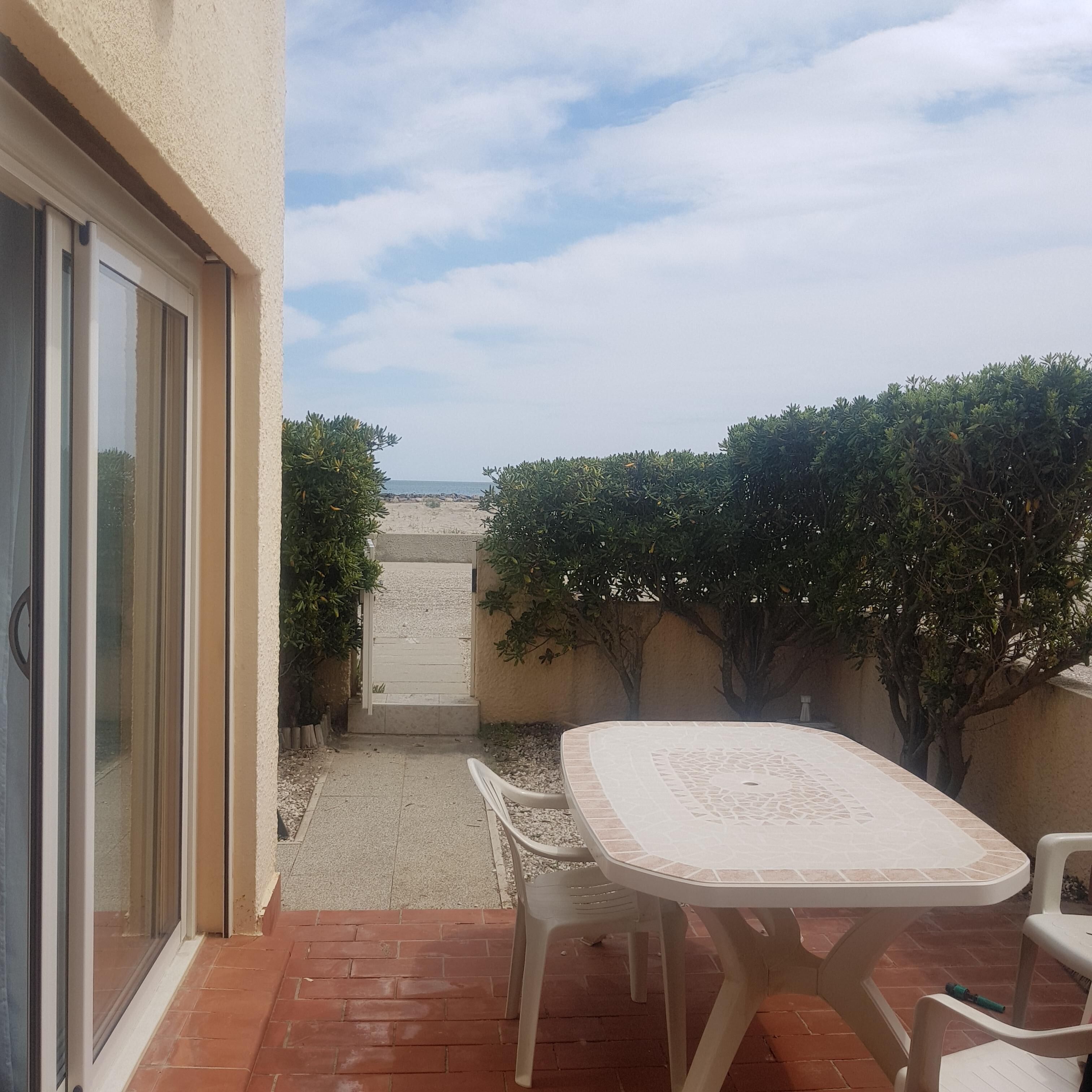 Un patio con una mesa y sillas, vista a la playa y una puerta que da a un área techada.