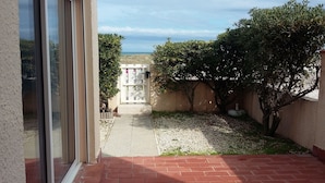 A patio with a red brick floor, a white door, and a view of the sea. - LARGE 3 BEDROOM APARTMENT ON THE SEAFRONT in quiet Barcarès just off the beach (Le Barcarès)