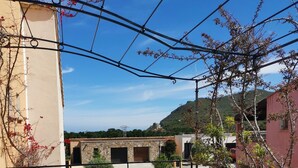 A balcony with a table and chairs, a view of a building with stone walls, and a mountainous landscape in the background. - New house in a touristy 3 stars residence in front of the sea (Belgodère)