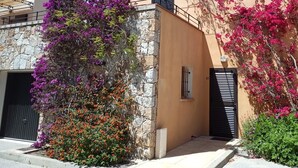 A building with a stone facade, a black gate, and vibrant purple bougainvillea flowers. - New house in a touristy 3 stars residence in front of the sea (Belgodère)