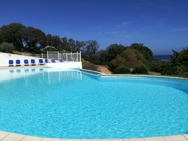 Una piscina azul cristalina con sillas de descanso azules y una valla blanca.