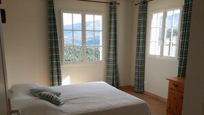 A bedroom with a bed, curtains, a dresser, and a window with a view of mountains. - Villa, near Ile Rousse and the sea, lake and mountain view (Santa-Reparata-Di-Balagna)
