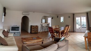 A living room with a sofa, coffee table, TV, dining table with chairs, and a kitchen area with cabinets and a refrigerator. - Villa, near Ile Rousse and the sea, lake and mountain view (Santa-Reparata-Di-Balagna)