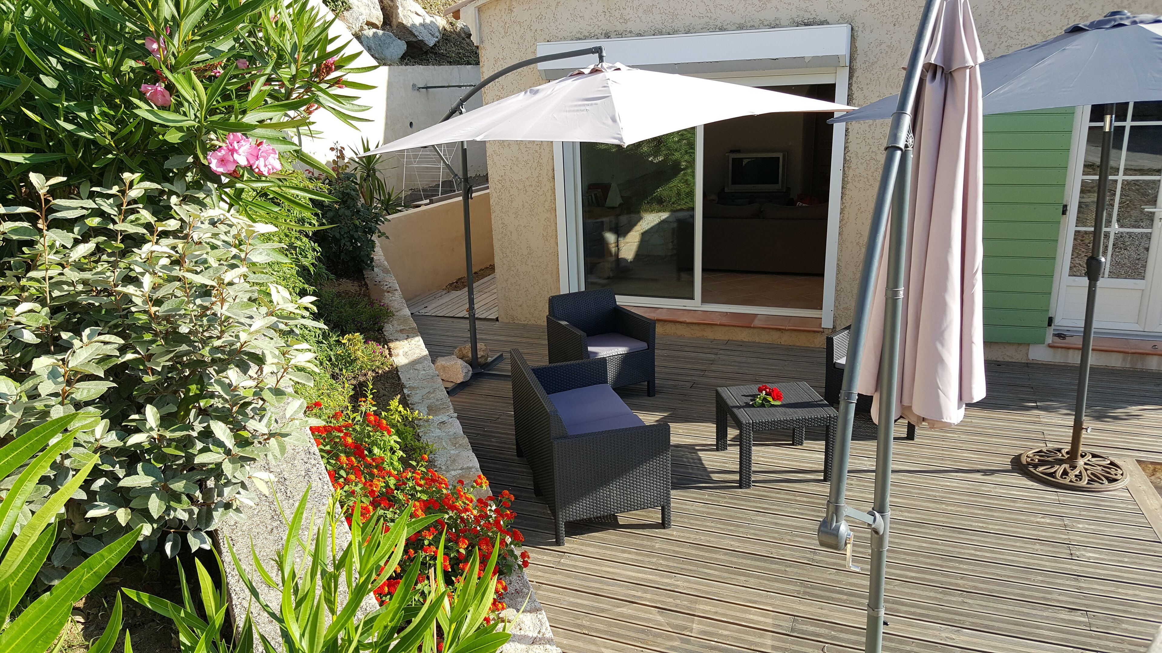 Una terraza de madera con muebles de mimbre y un paraguas blanco.