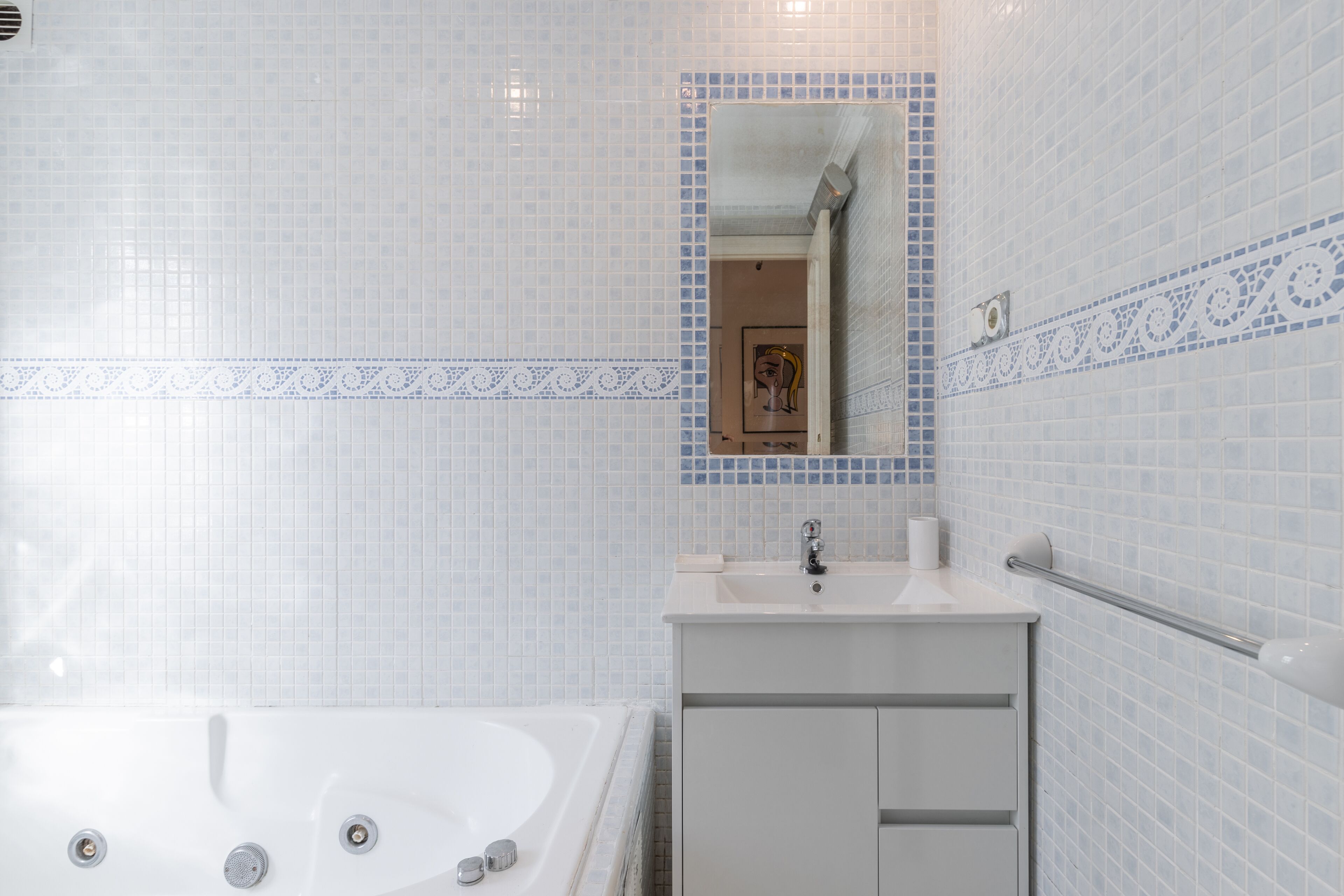 Une salle de bain avec une baignoire blanche, un lavabo avec un miroir et des murs carrelés.