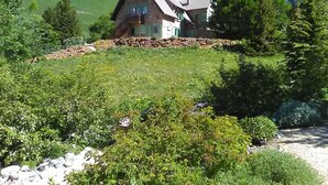 A stone building with a sloped roof, surrounded by lush greenery and a mountain backdrop. - Apartment, garden level, with mountain views, close to the center.  (Briançon)
