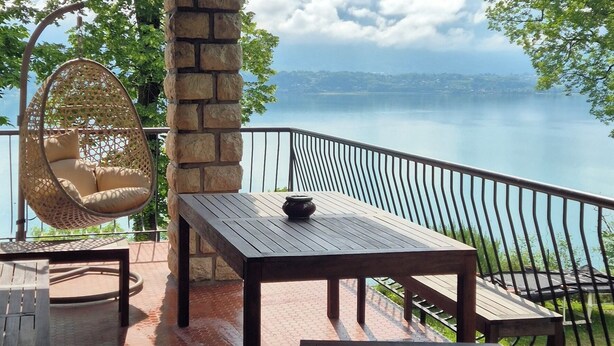 Eine überdachte Terrasse mit Seeblick, ausgestattet mit einem Tisch, Stühlen und einer Hängematte.