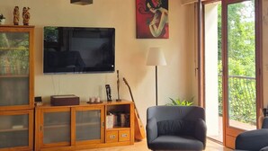 Ein Wohnzimmer mit Flachbildfernseher, Holzschnitzschränken, einer Gitarre und einem Balkon mit Blick.