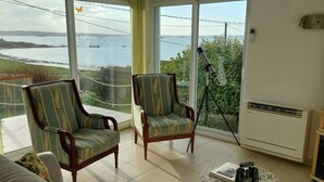Ein Wohnzimmer mit einer Couch, zwei Sesseln, einem Teleskop und Blick aufs Meer.