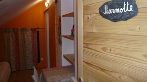 Una habitación acogedora con una puerta de madera que dice 'Harmotte', una mesita con mantel floral y una silla.